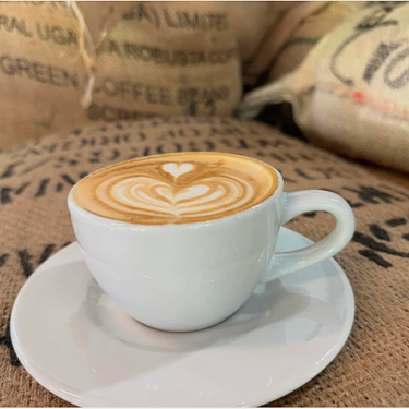 Latte art in a white cup on burlap coffee sacks.
